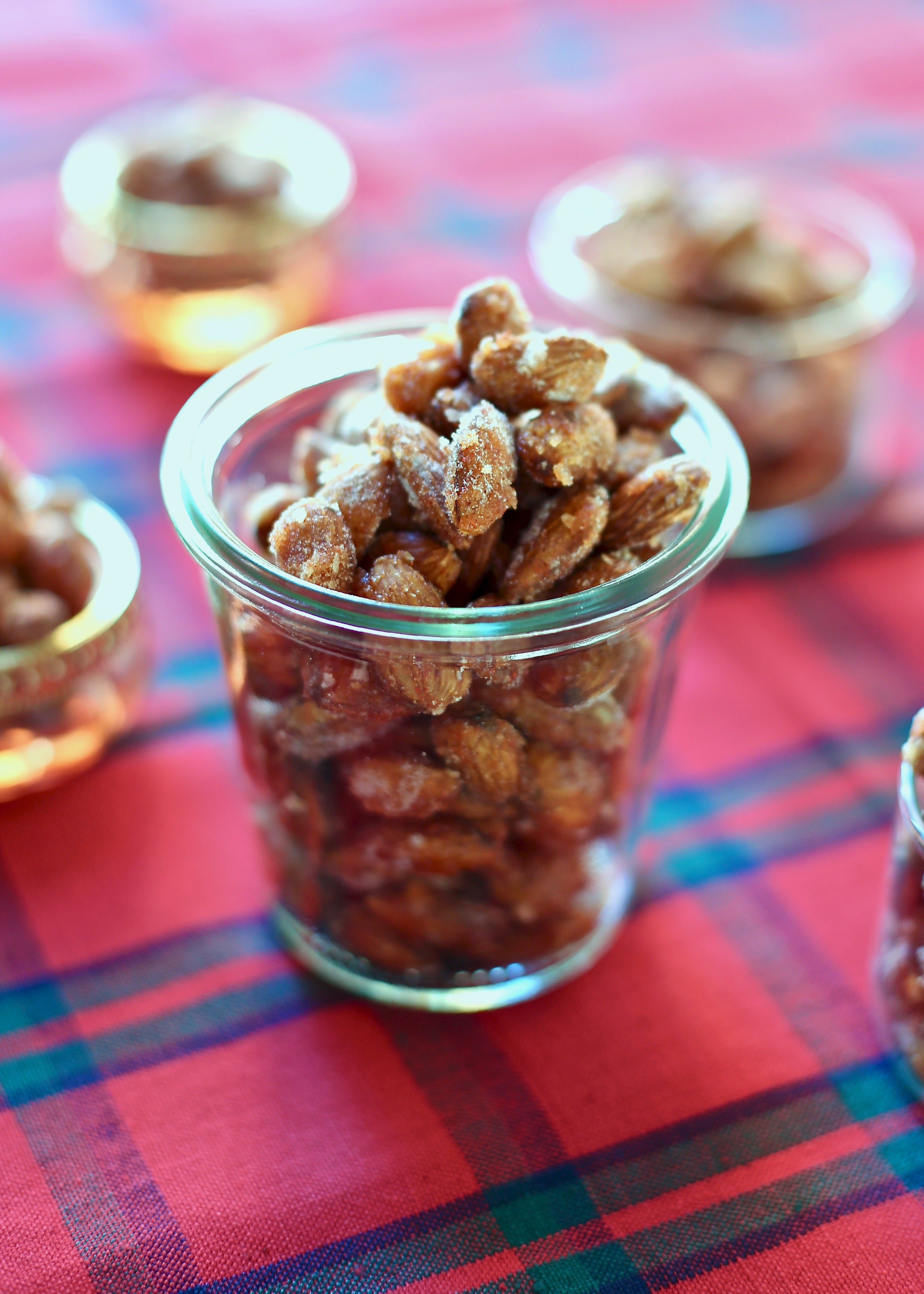 Almonds that are for snacking in a glass jar on a red tablecloth