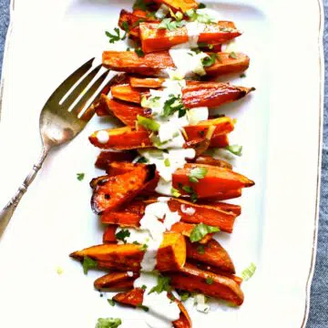 a white platter with a serving fork of roasted sweet potatoes.