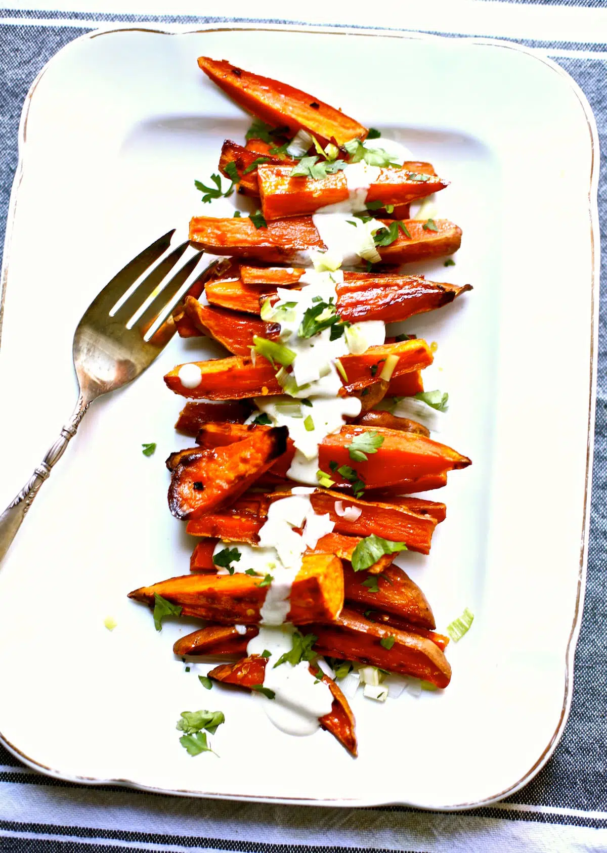 a white platter with a serving fork of roasted sweet potatoes.