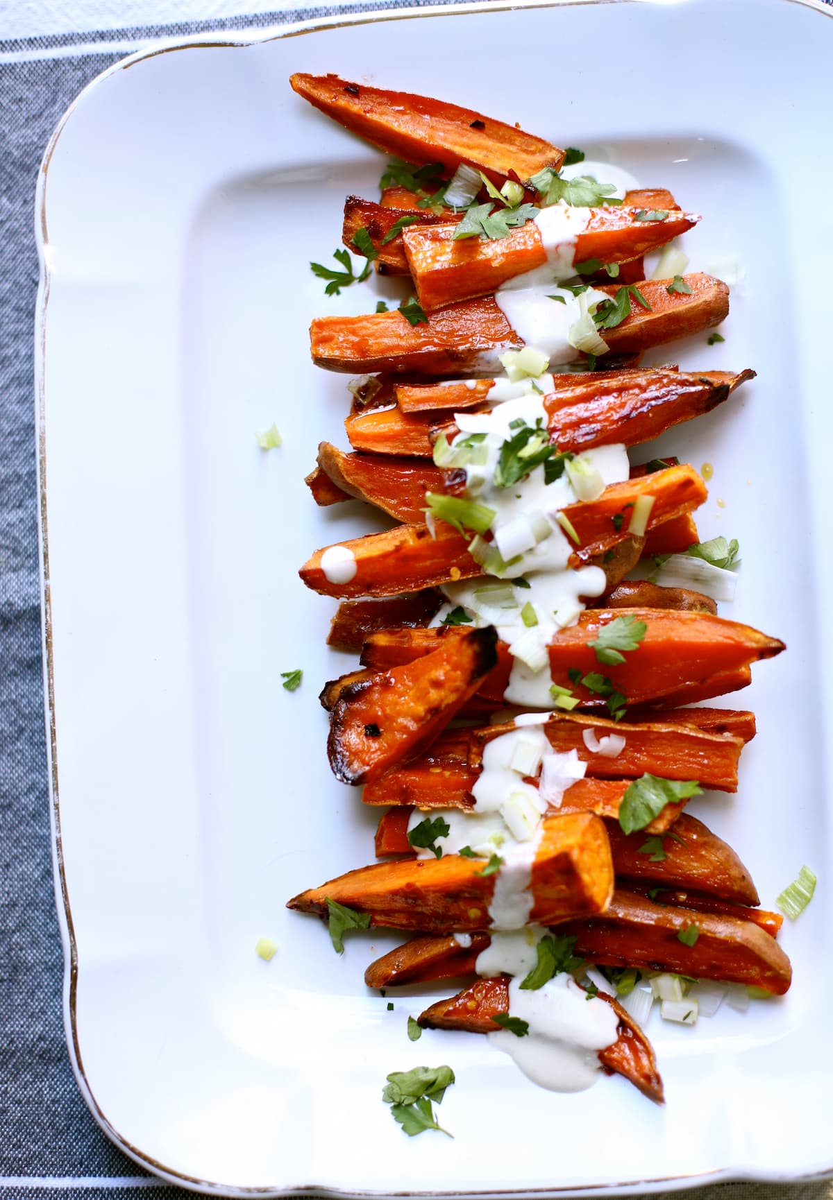 a white platter of roasted sweet potatoes with a white yogurt sauce on them.