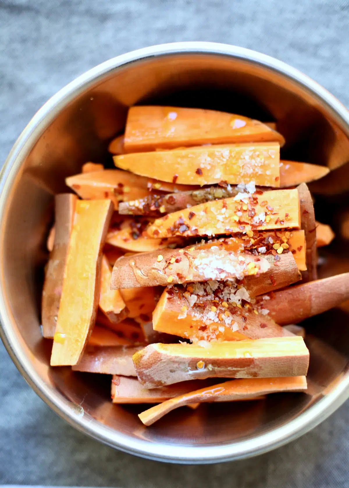 a bowl of cut and raw sweet potatoes with spices on top.