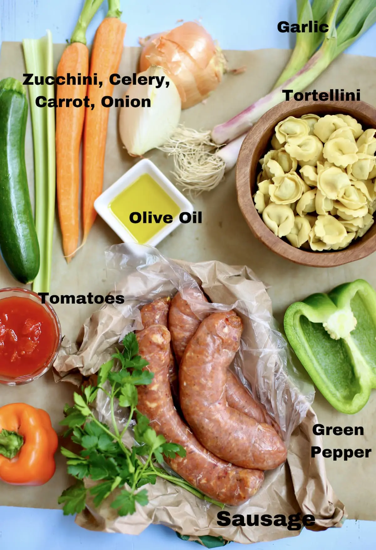 a grouping of ingredients for soup, vegeatables, tortellini and chicken sausage with a text overlay saying what the ingredients are