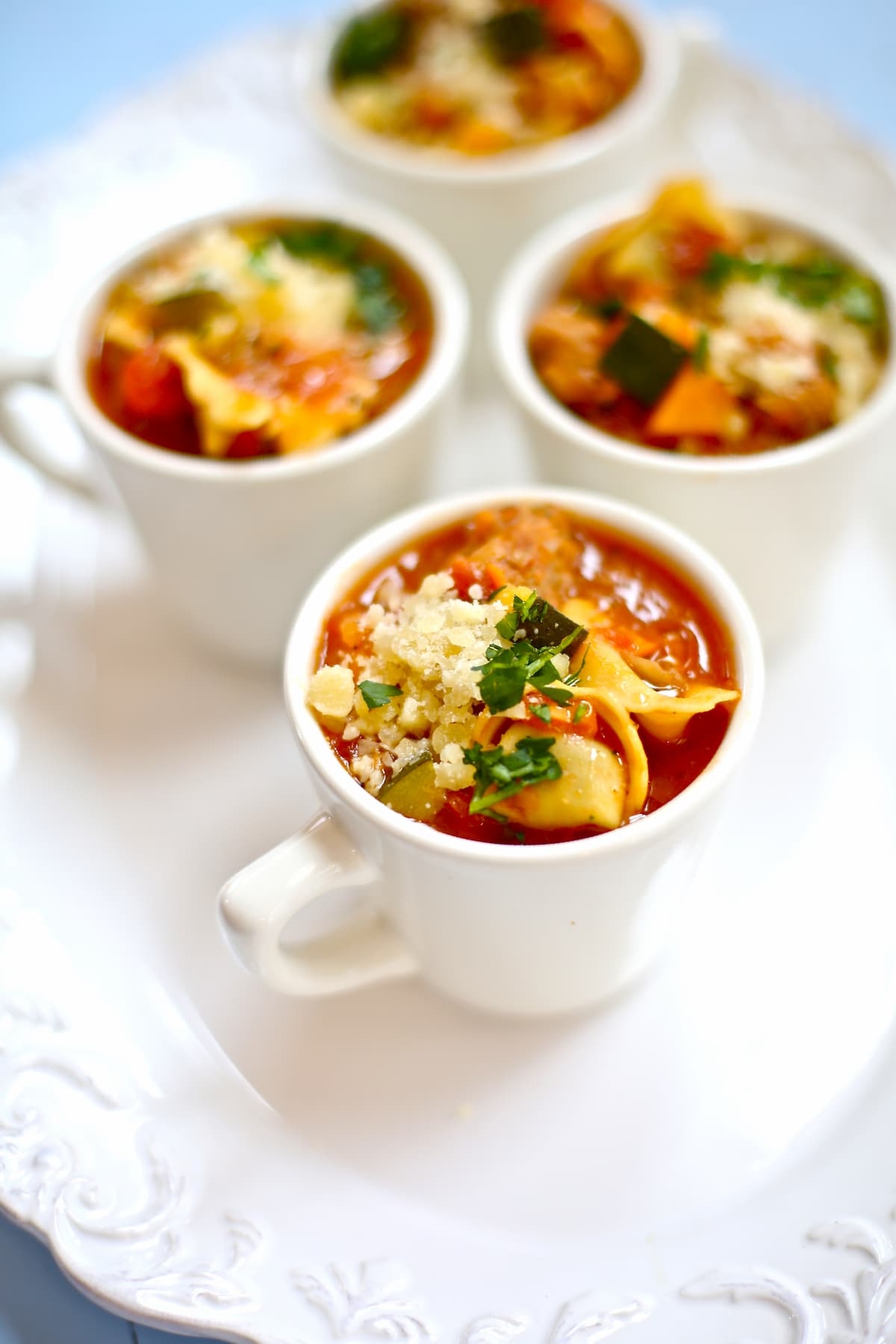 three cups of chicken sausage tortellini soup in white cups on white background on a white table