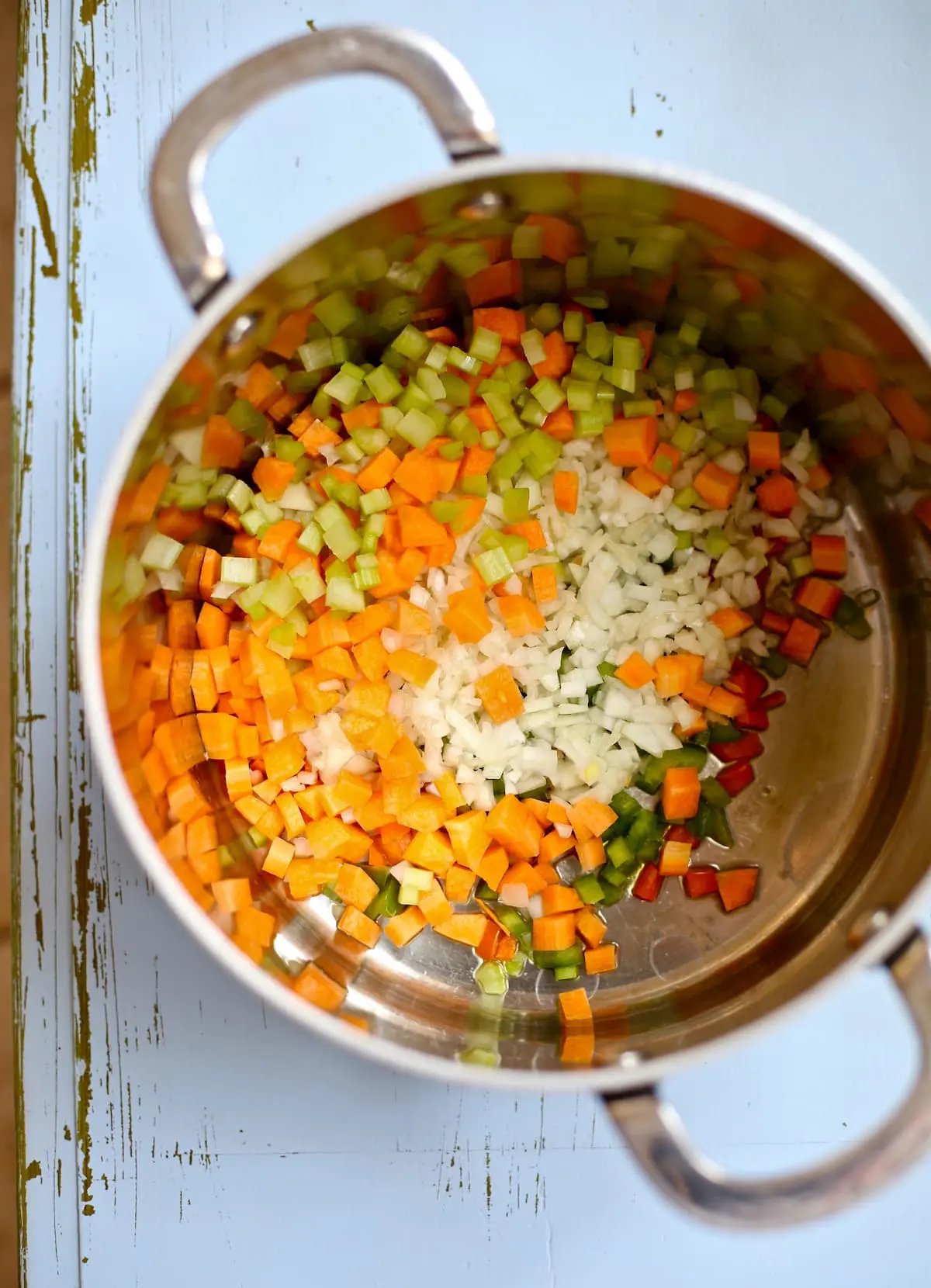a dutch oven with carrots, celery and onion in it, chopped, on a blue table