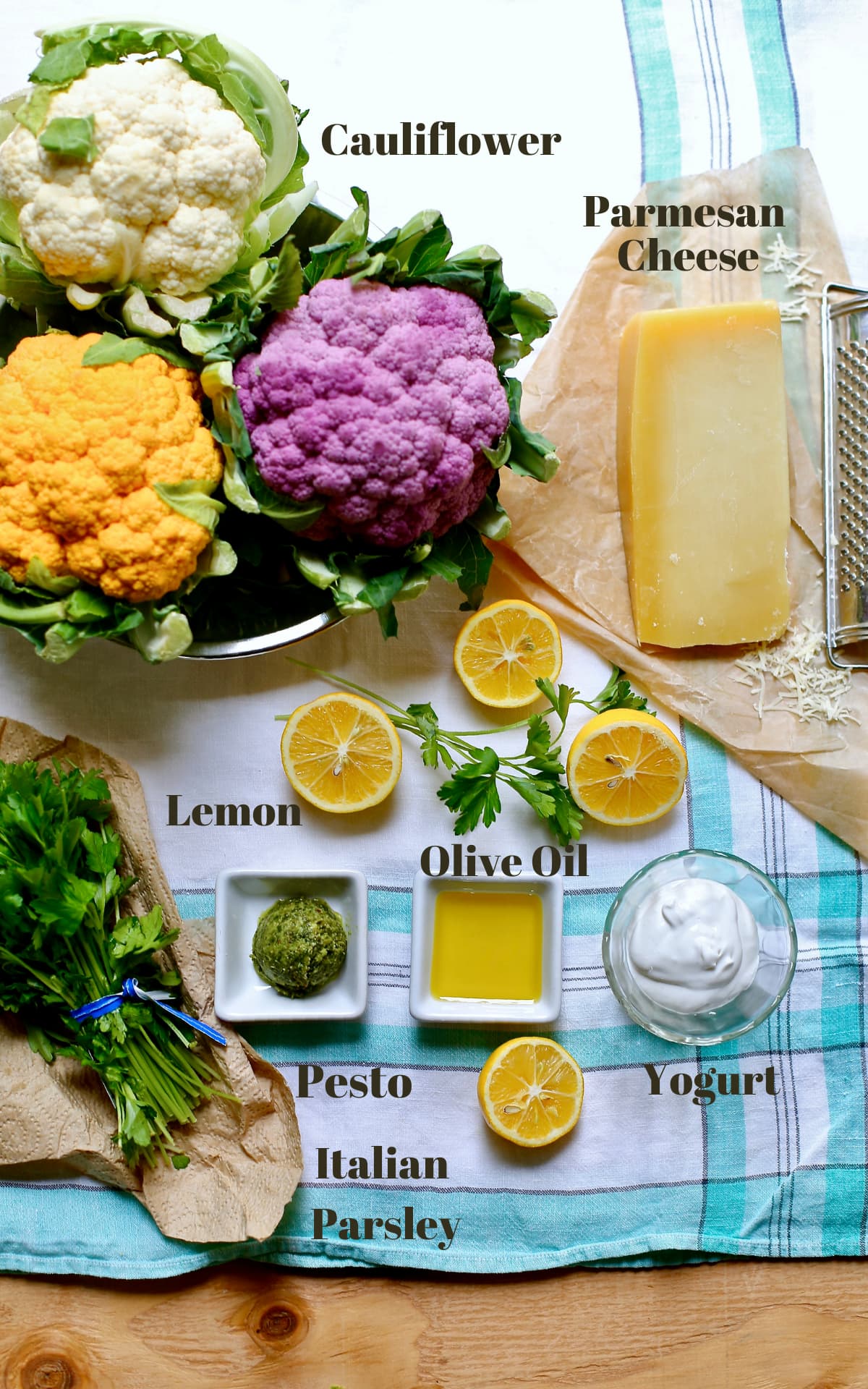 a cutting board with a list of ingredients needed for a recipe.Cauliflower, olive oil, Parmesan cheese, lemon and parsley, yogurt and pesto. 