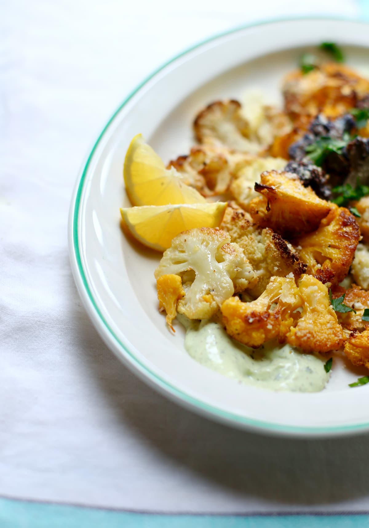 a side shot of a plate of roasted cauliflower with yogurt sauce with a lemon wedge onthe side of the plate.
