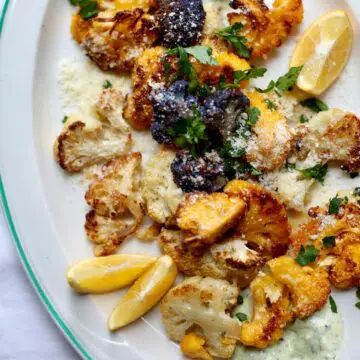 a white platter of roasted cauliflower with some lemon wedges on the side.