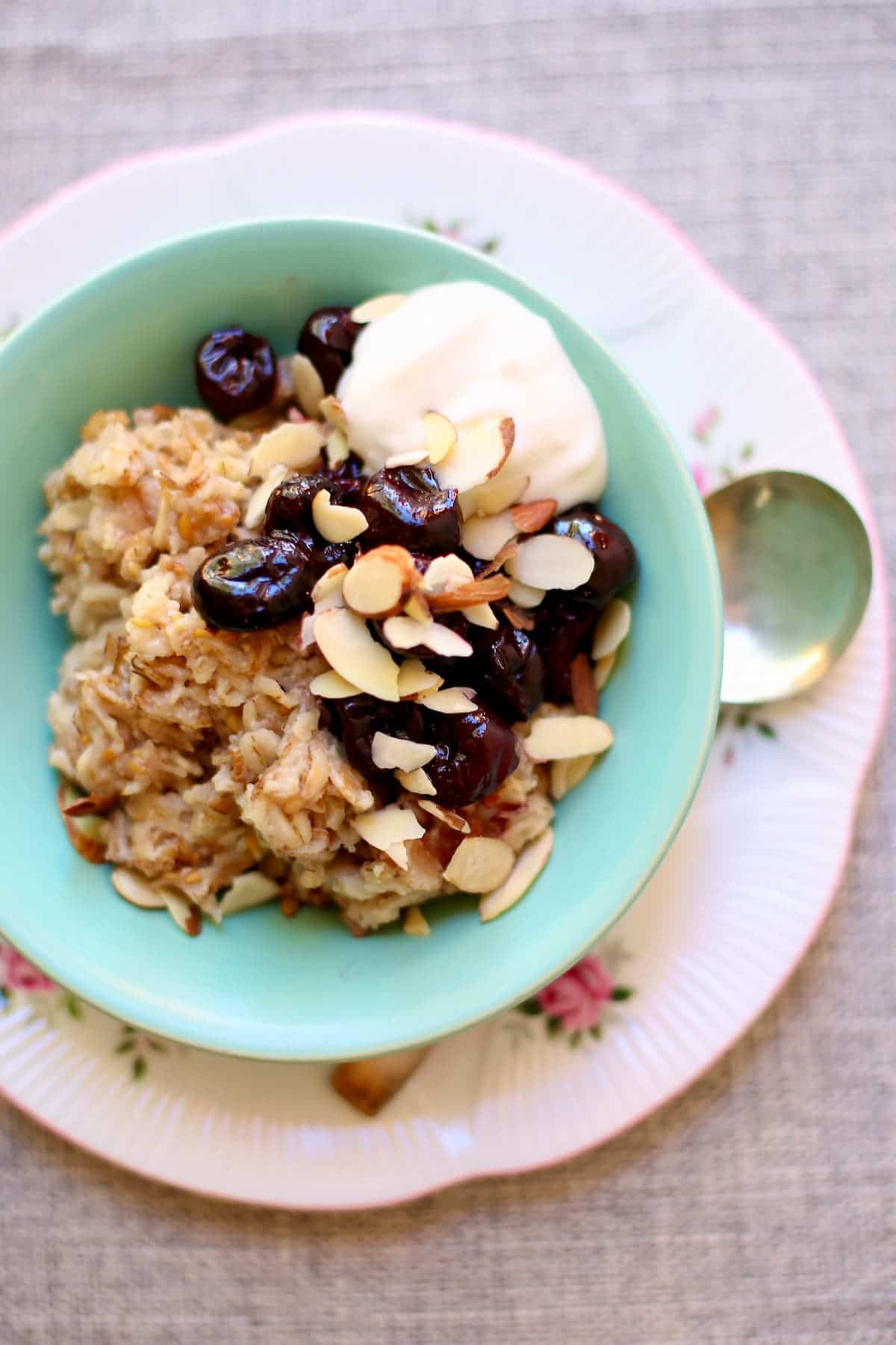 a photo of a bowl of oatmeal with cherries on top and plain yogurt and sliced almonds.