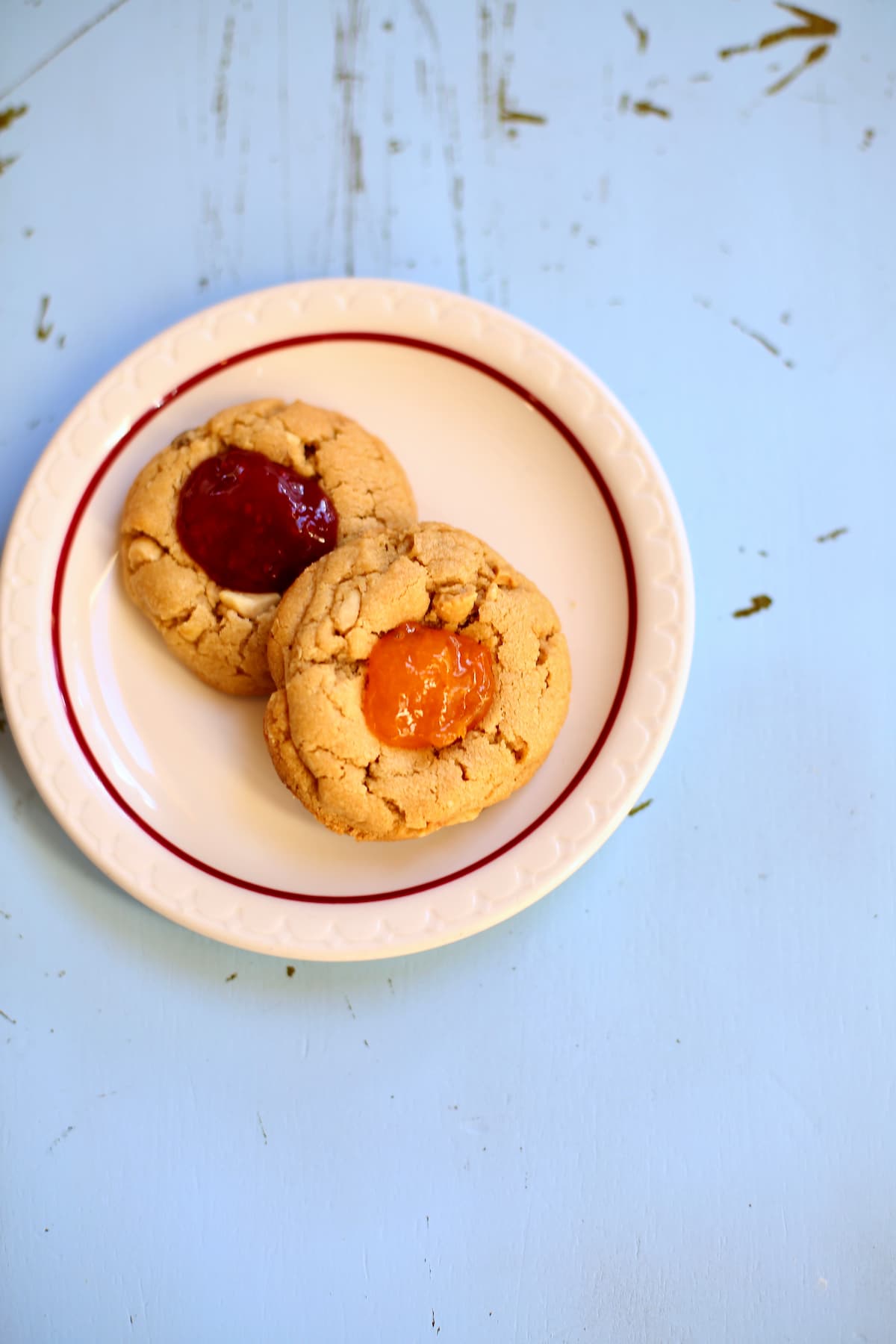 Peanut Butter and Jam Cookies a blue table with a plate of cookies on it.