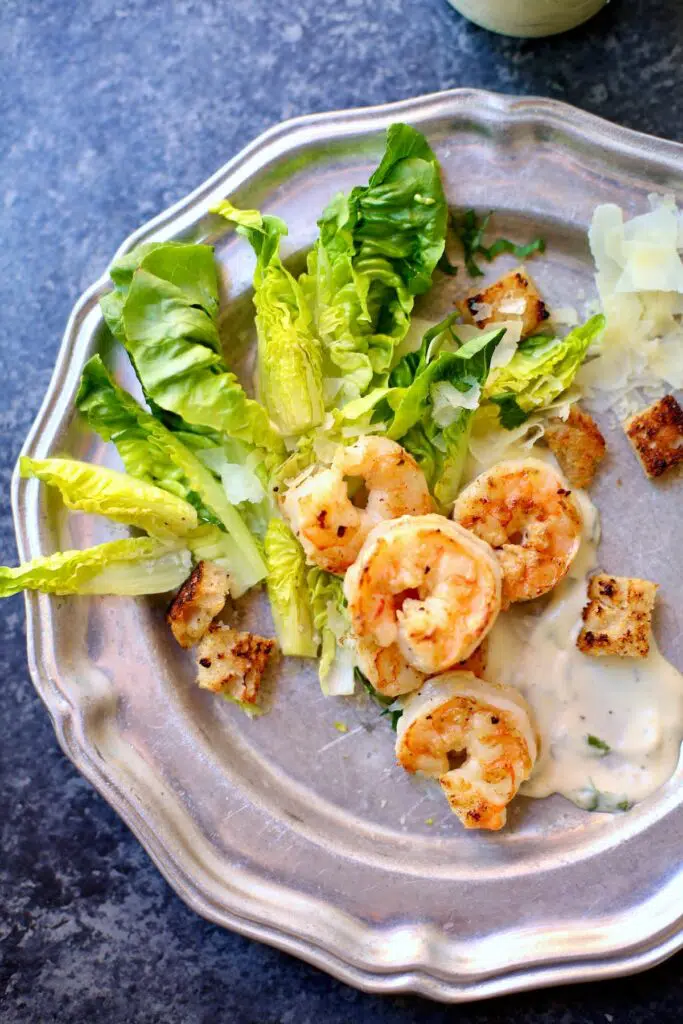 a shrimp and greens salad on silver plate on a blue table.