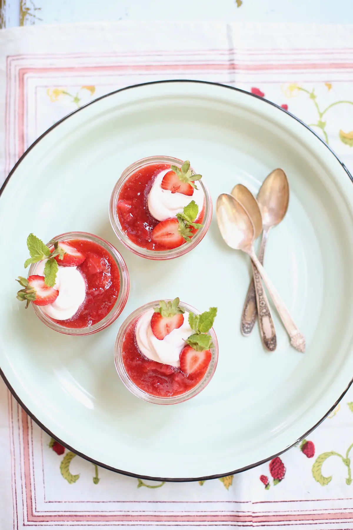 three strawberry cheesecakes in a jar with spoons on a blue platter 