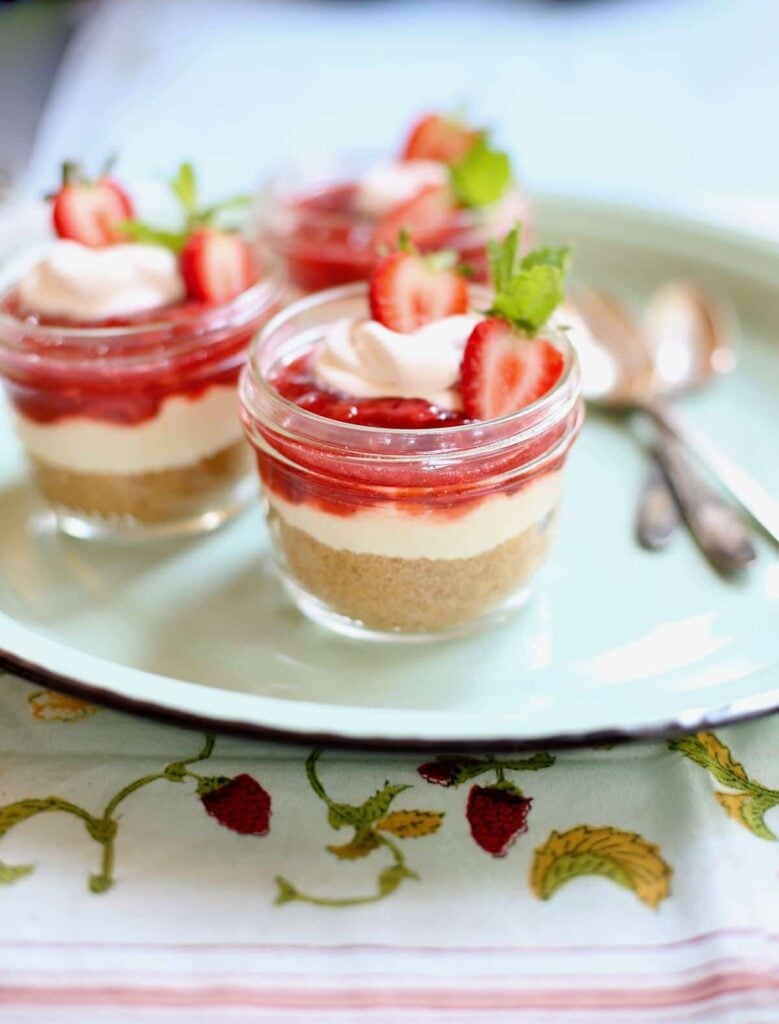 three strawberry cheesecakes with spoons on a blue platter 