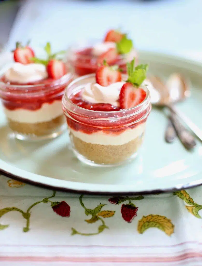 three strawberry cheesecakes with spoons on a blue platter