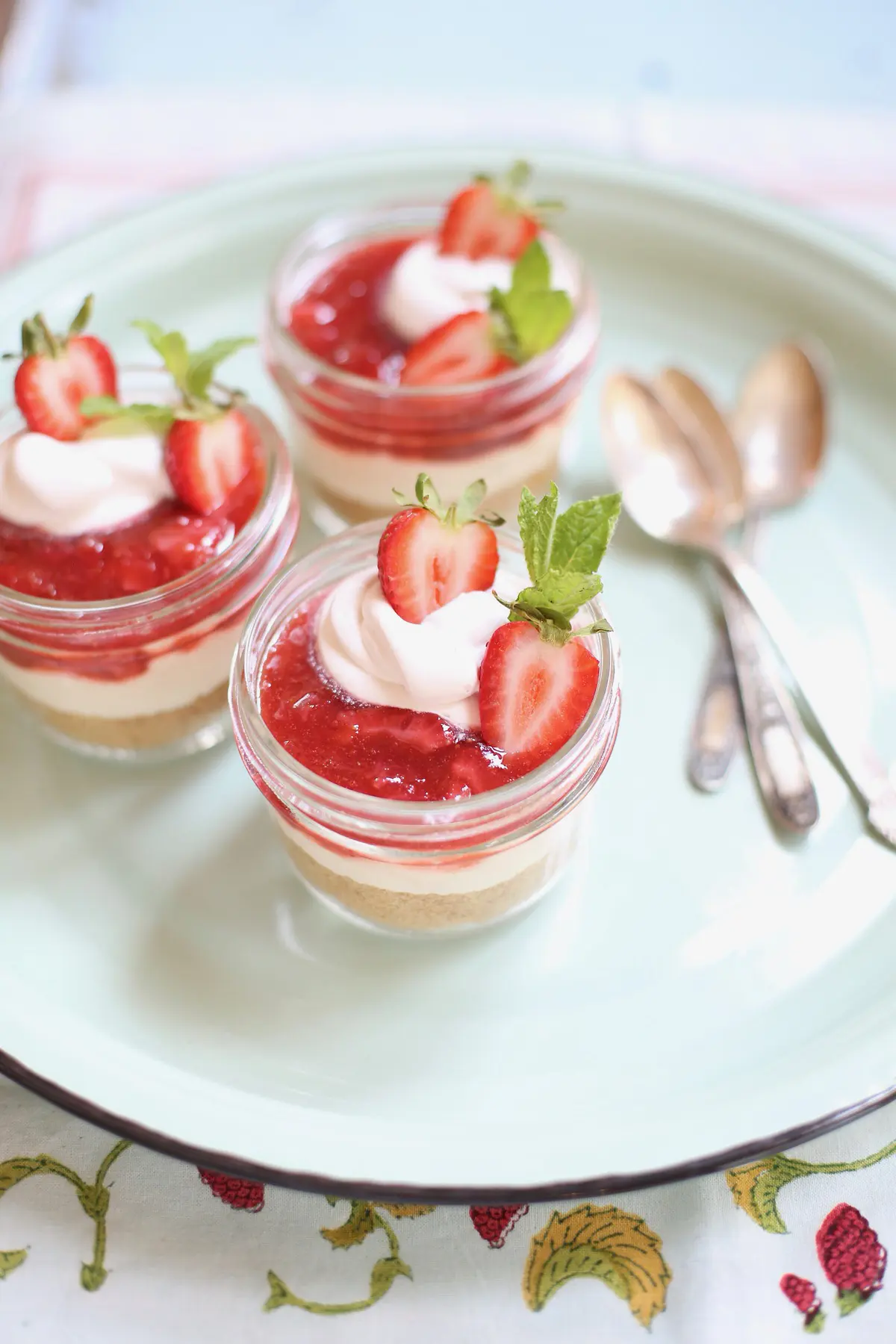 three strawberry cheesecakes in a jar with spoons on a table