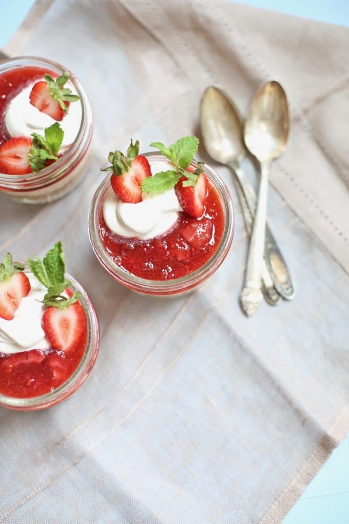 three strawberry cheesecakes in a jar with 3 spoons 