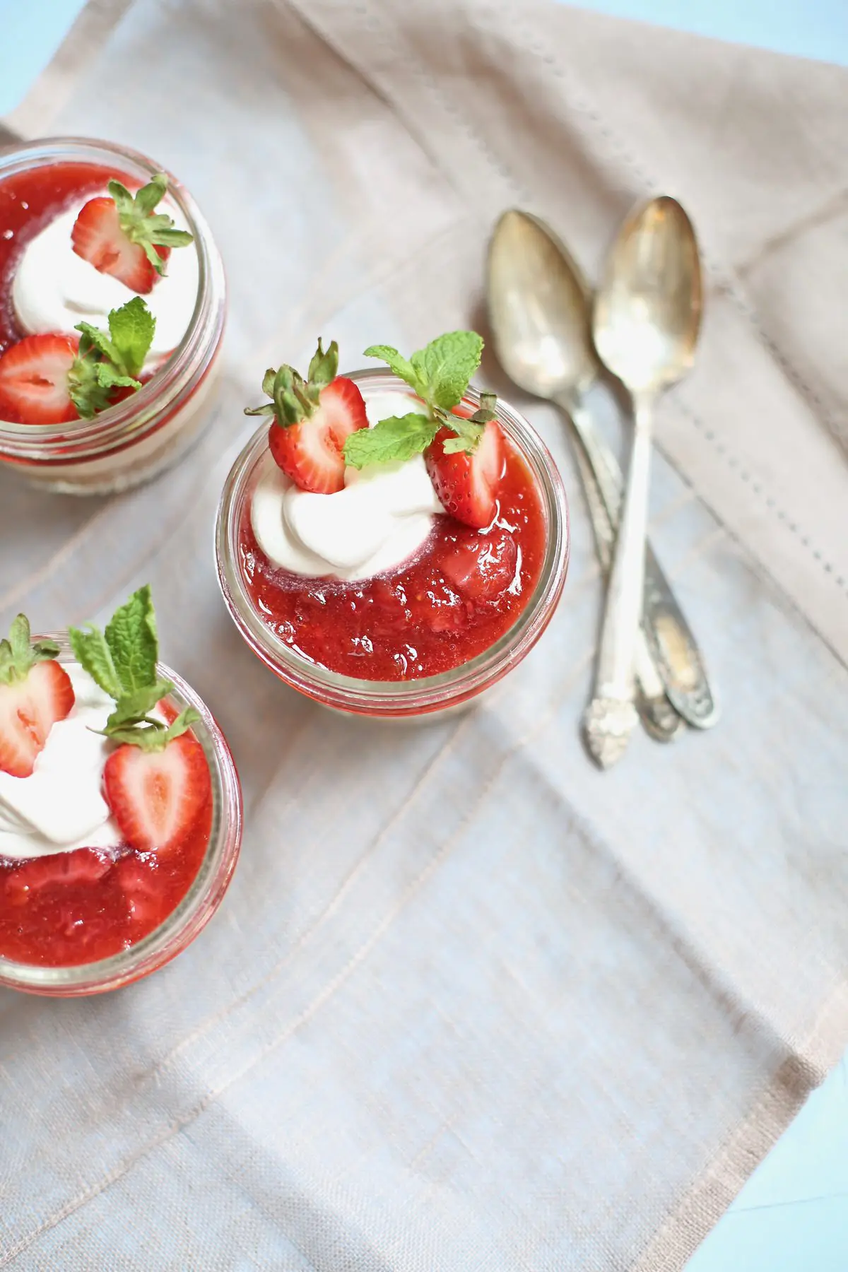 three strawberry cheesecakes in a jar with 3 spoons