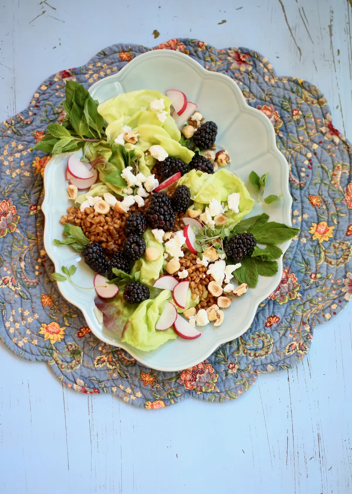 Long blue platter of salad made of goat cheese, blackberries, hazelnuts, radish and mint on a blue table 
