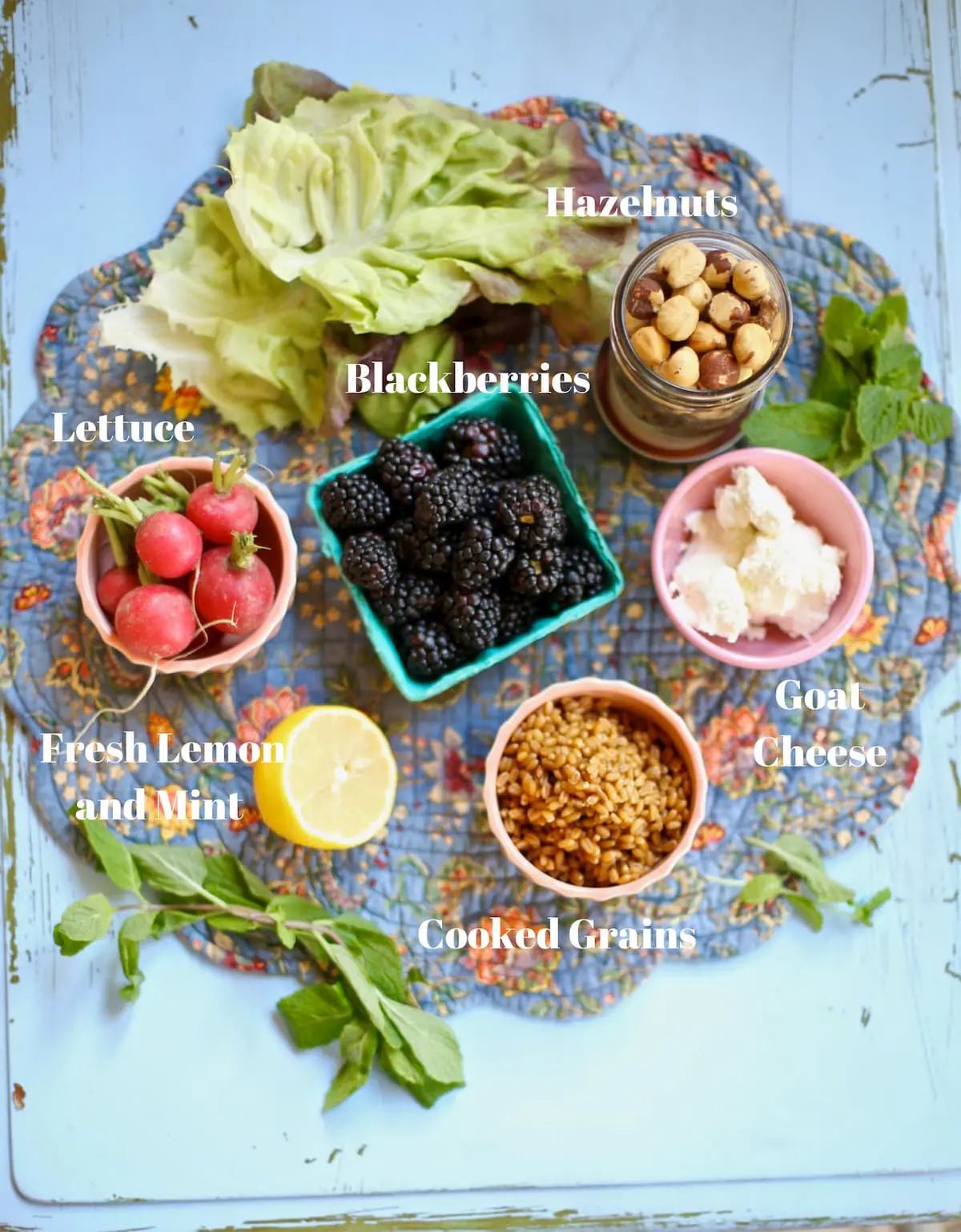 Ingredients for blackberry salad with white text overlay on a blue fabric place mat.