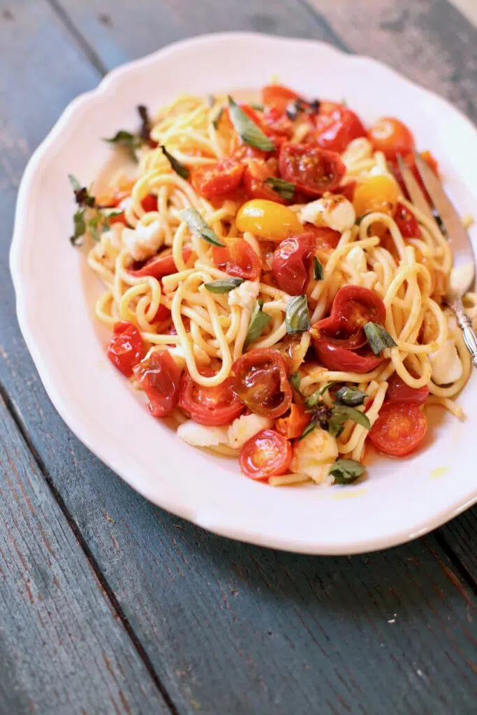 Pasta with tomatoes on a white plate and blue table