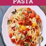 pasta with tomatoes on a white plate with a fork on a table