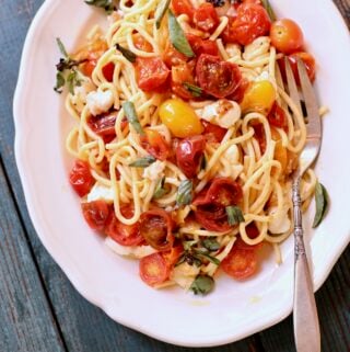 pasta with tomatoes on a white plate and blue wooden table