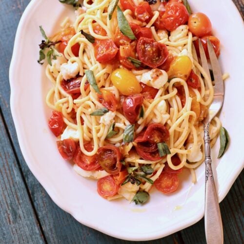 pasta with tomatoes on a white plate and blue wooden table