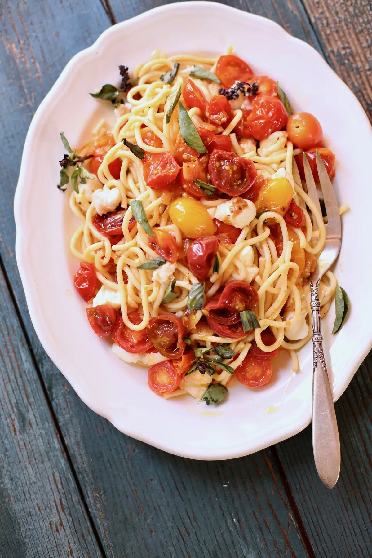 pasta with tomatoes on a white plate and blue wooden table