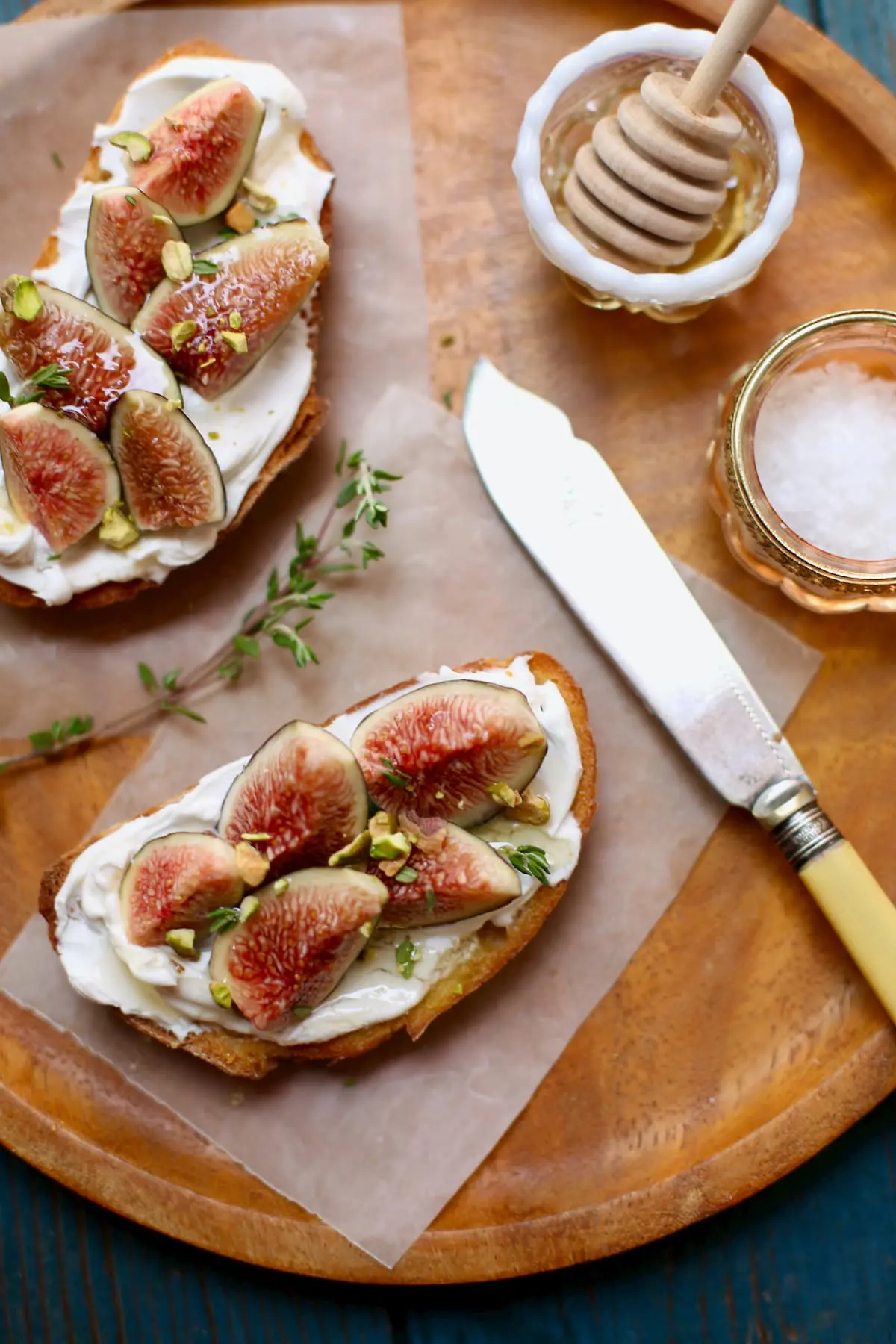 Fig toasts on a wooden plate with yellow knife and salt and honey