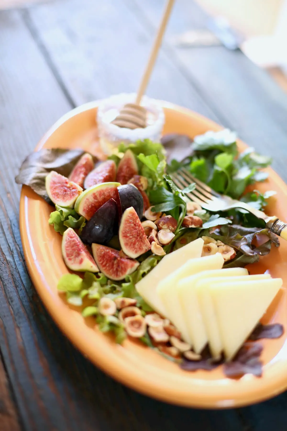 Figs, cheese and hazlenuts and honey on an orange platter