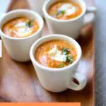 three white coffee mugs with pumpkin soup in them, on a wooden tray. with a text overlay saying the recipe name.