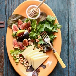 figs and greens and cheese and honey and a fork on a platter