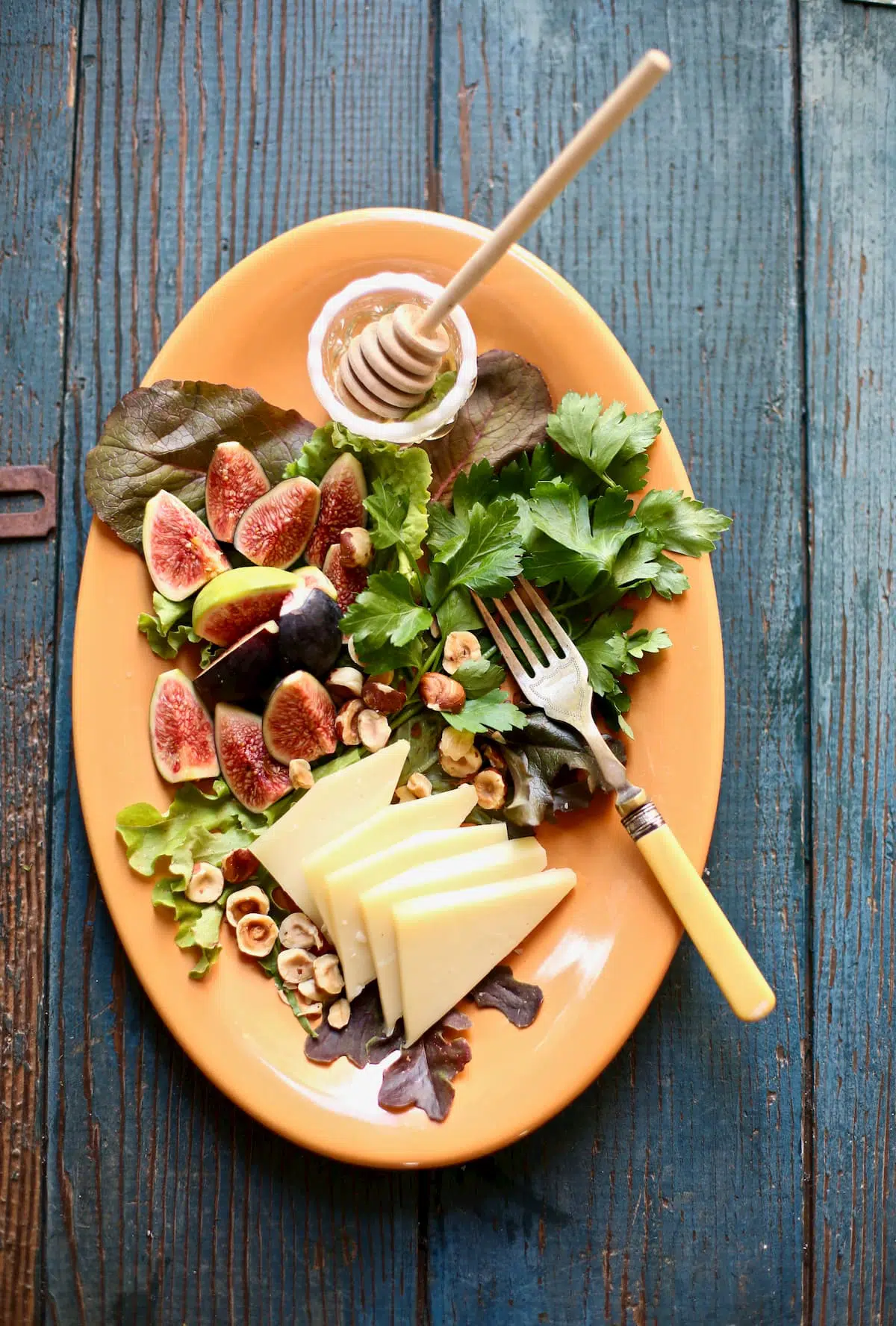 figs and greens and cheese and honey and a fork on a platter