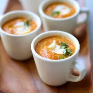 a grouping of pumpkin soup in small white cups with text overlay saying the recipe name.