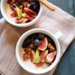 Two white bowls of yogurt and figs on a blue table