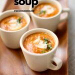 a few cips of pumpkin soup in white mugs on a serving plate.