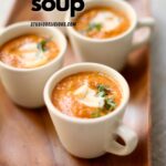 a few cips of pumpkin soup in white mugs on a serving plate.