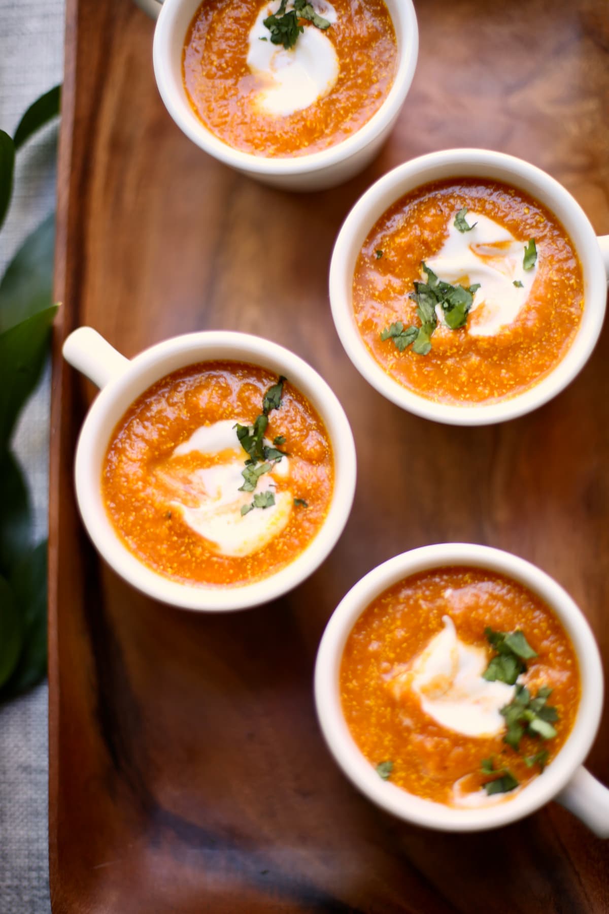 four white coffee cups of soup on a wooden plate.