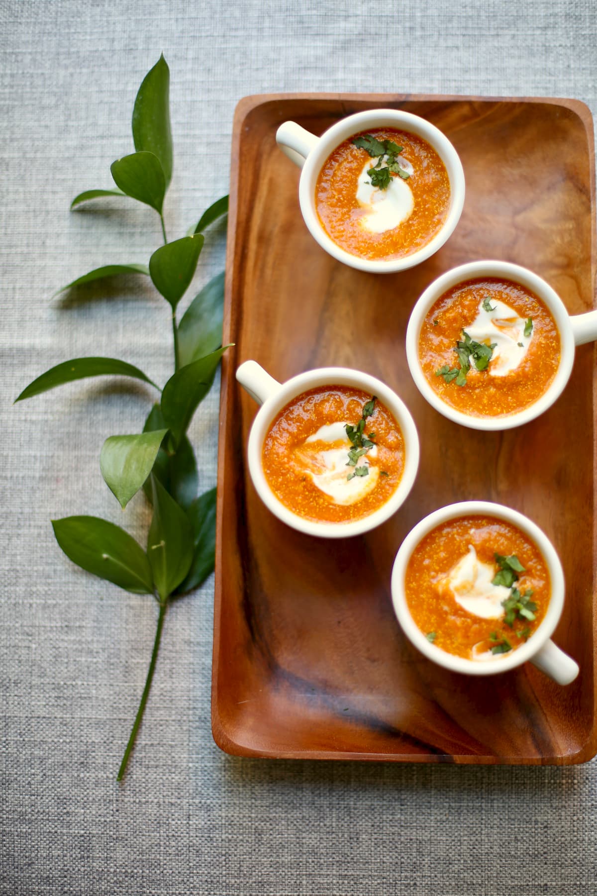 four cups of soup on a serving tray with greenery next to it.