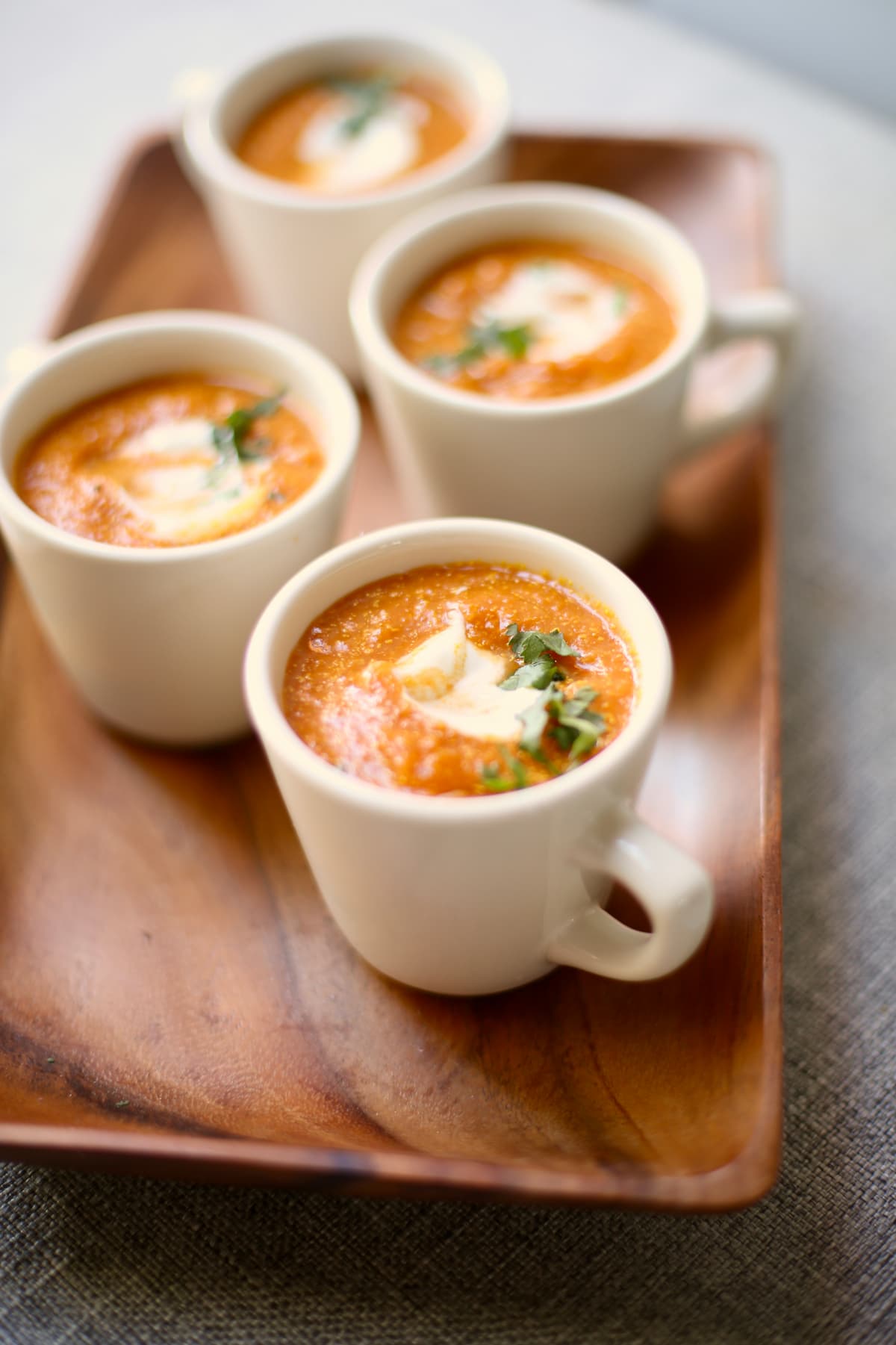 Cups of pumpkin soup on a wooden serving tray. 