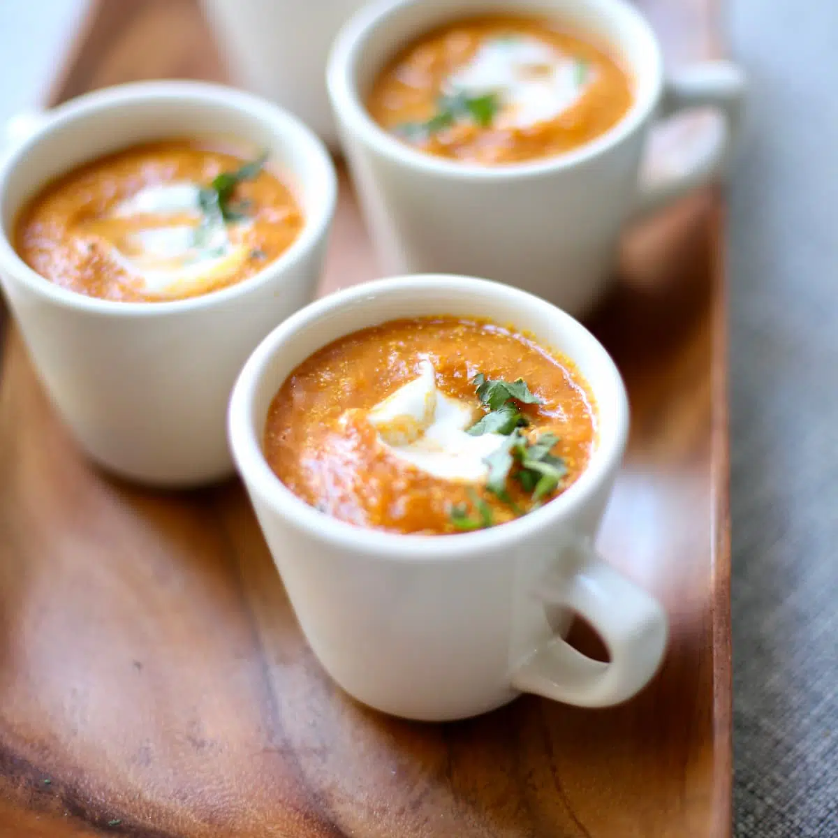 several cups of pumpkin soup in white cups on a wooden serving tray.