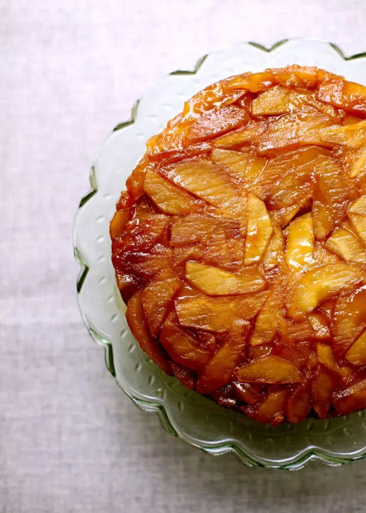 a picture of an apple cake on a green glass stand on a gray table.