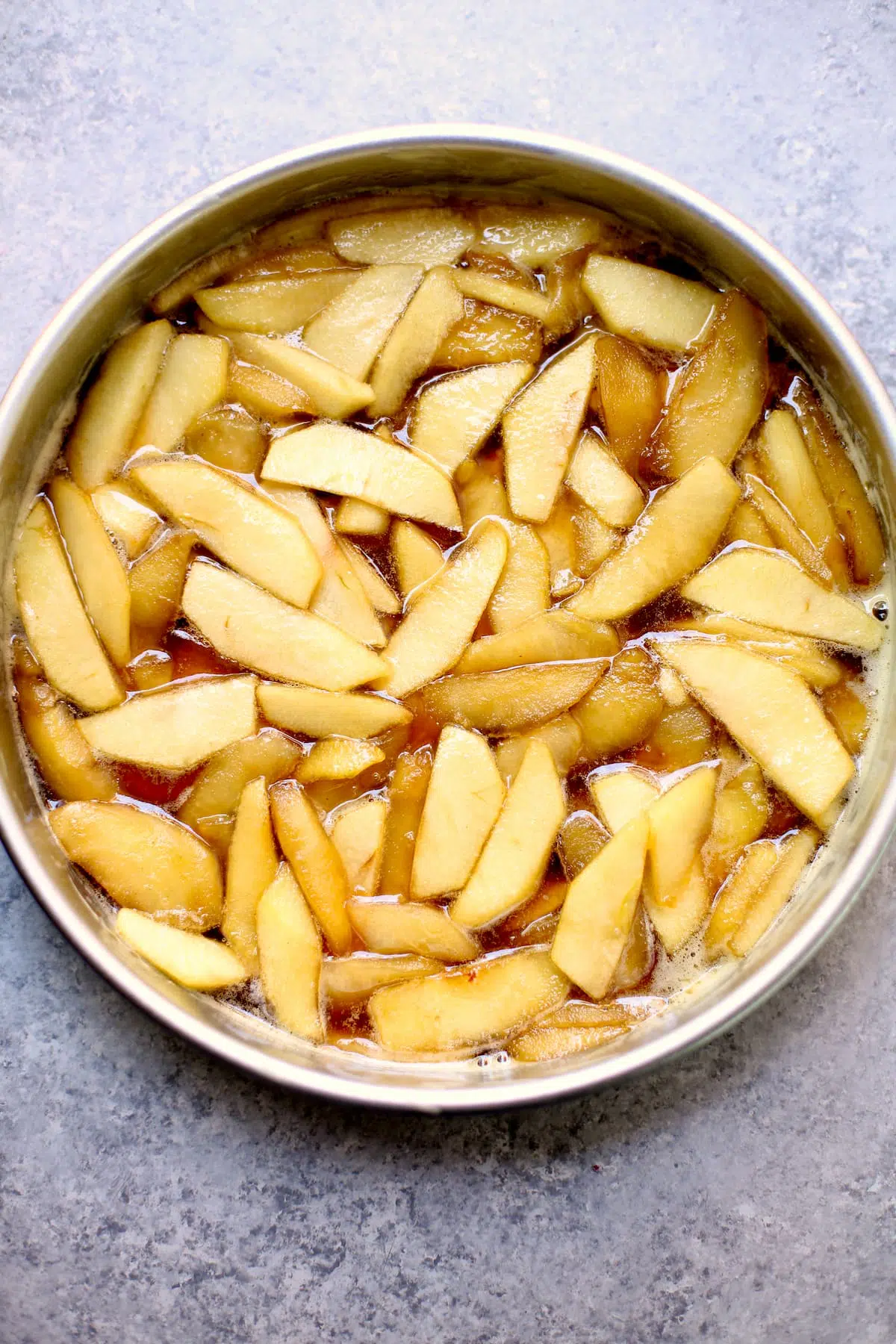 a round baking pan with raw sliced apples on a gray table.