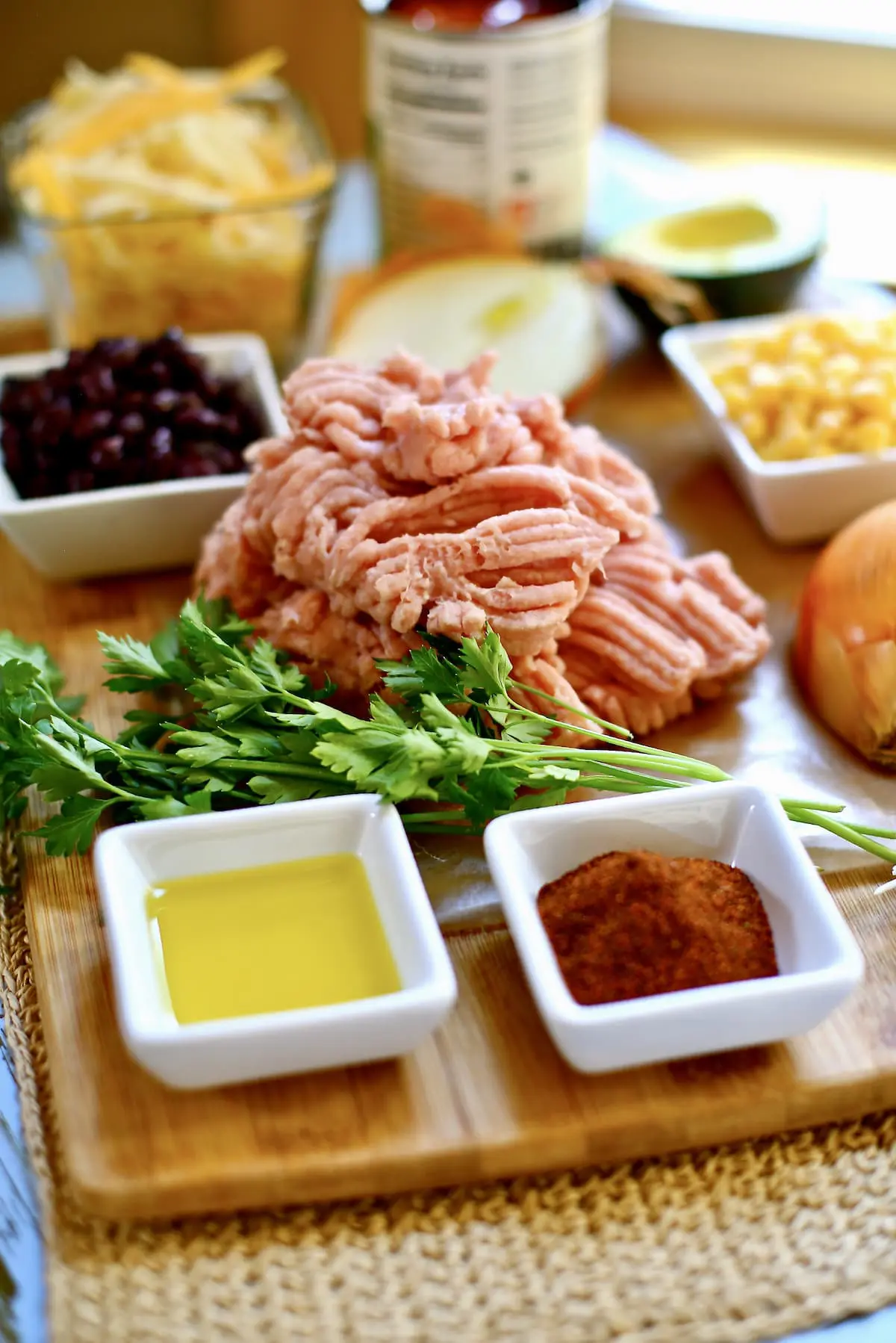 ingredients on a wood cutting board, ground turkey, spices, olive oil black beans and onion.