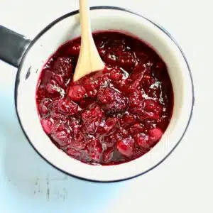 A white saucepan with cranberry sauce in it and a wooden spoon.