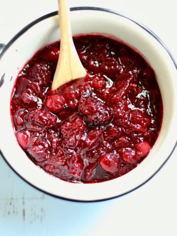 A white saucepan with cranberry sauce in it and a wooden spoon.