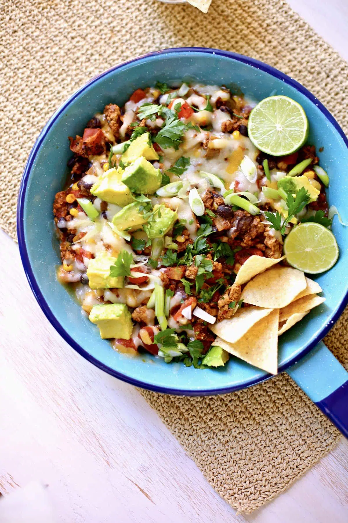 a blue skillet with cooked taco meat with melted cheese, chips, lime and avocado.