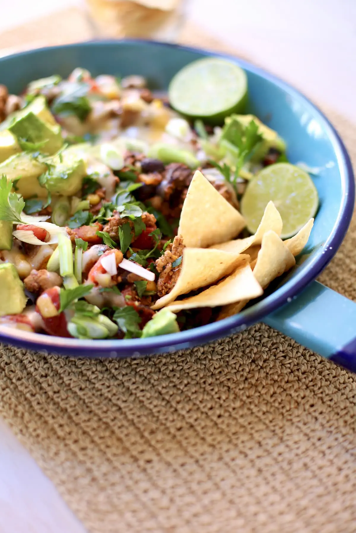 a blue skillet with taco meat, chips, lime and avocado