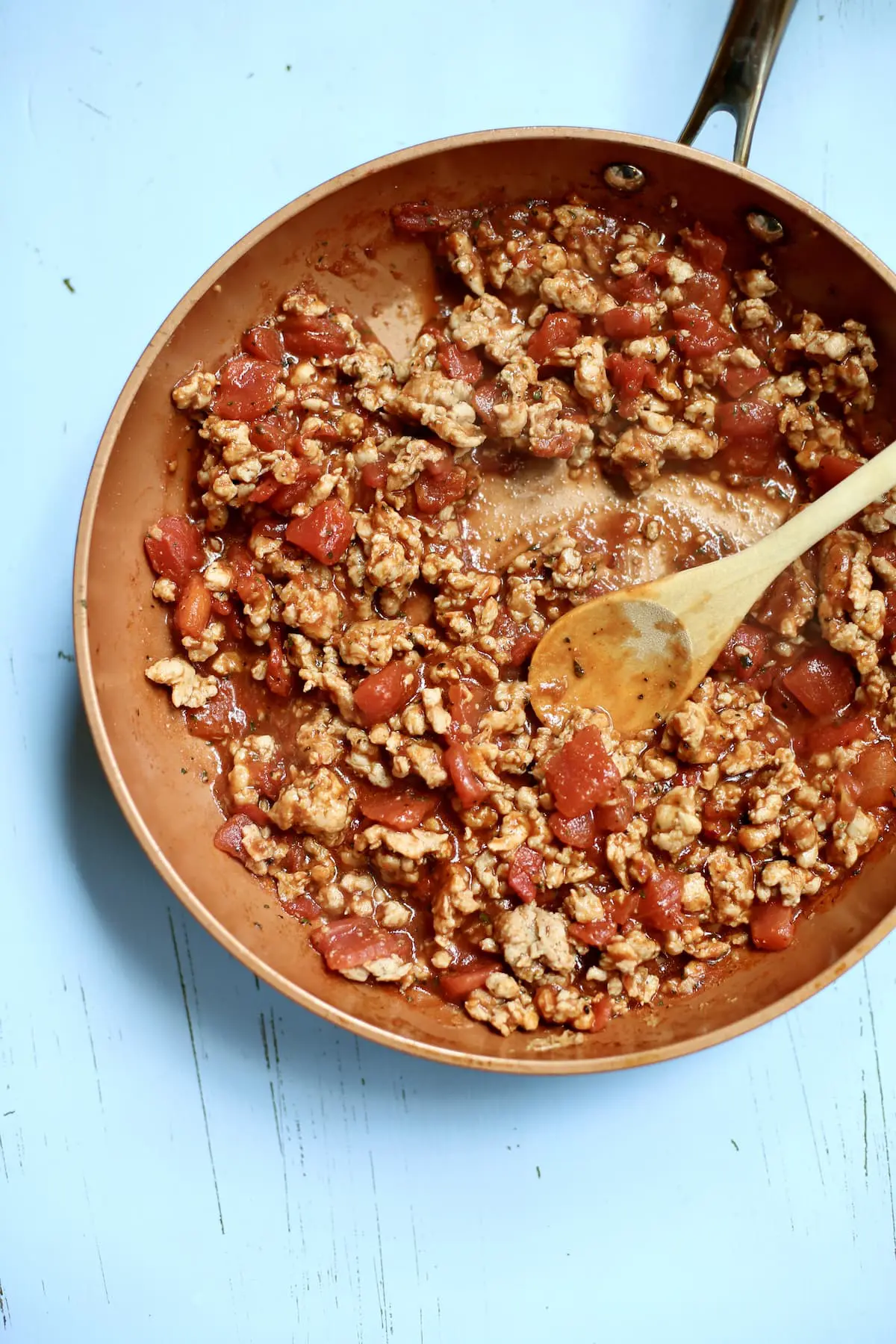 a skillet of cooked taco meat on a blue table with a wodden spoon.