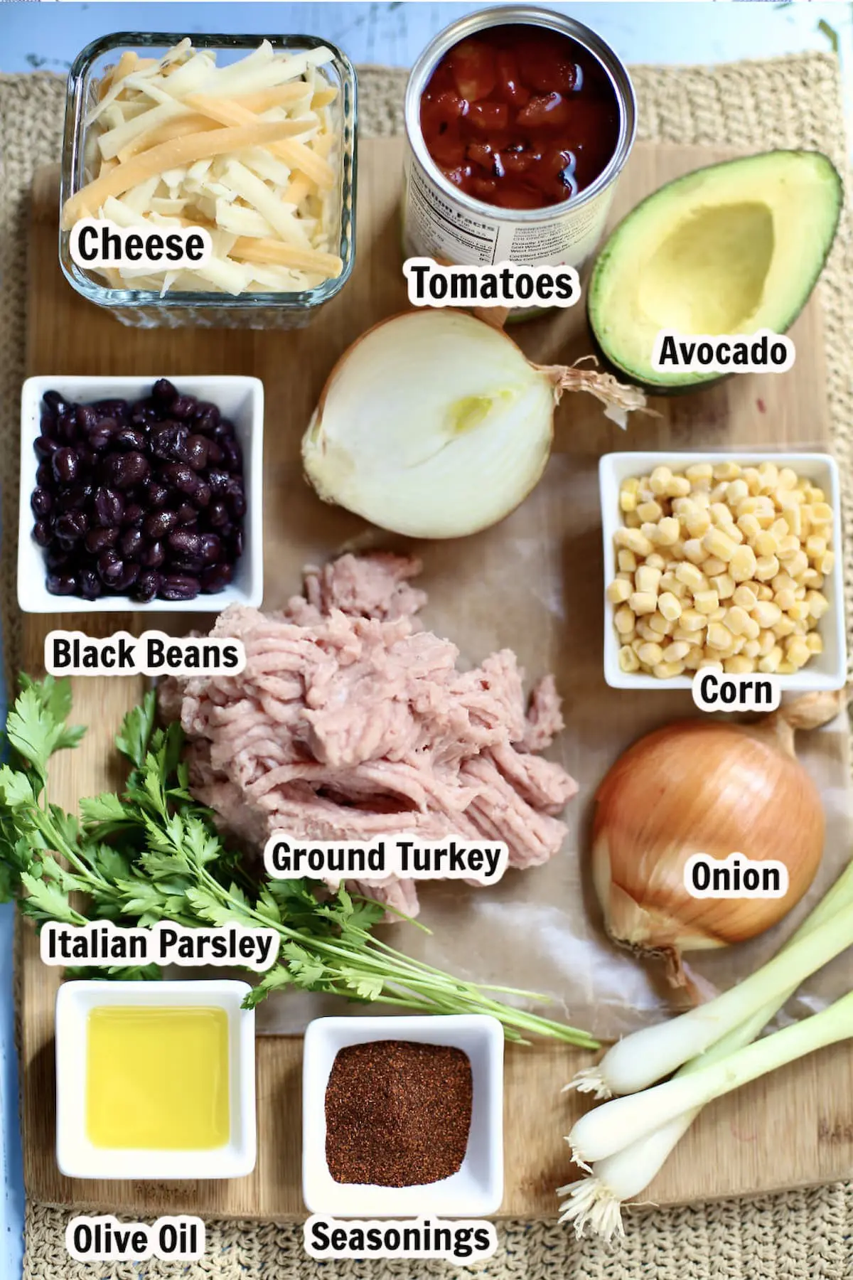 ingredients for a recipe marked with text overlay. Ground turkey, onion, black beans, cheese, avocado and corn.