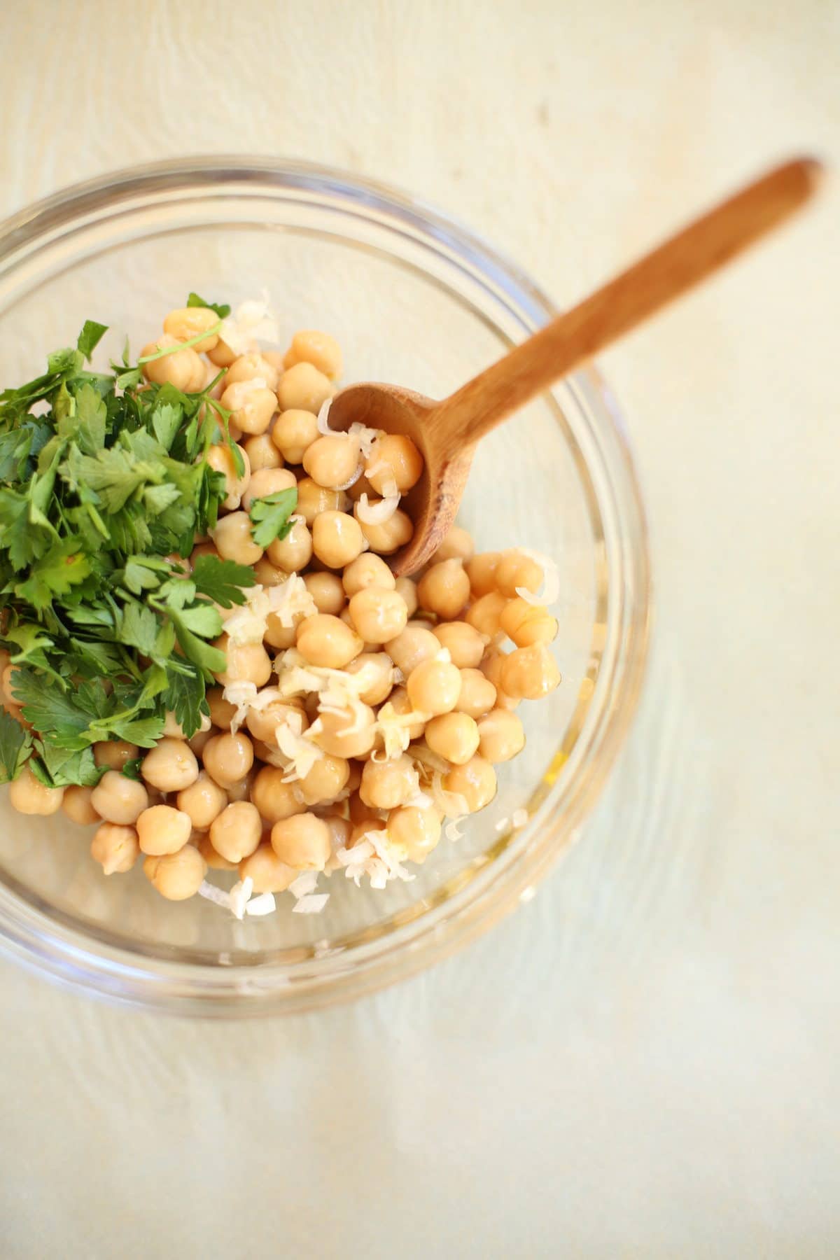 chickpeas and parsley in a glass bowl with wooden spoon